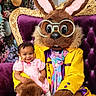 child, toddler, costume, bunny, mascot, purple_throne, glasses, yellow_jacket, pink_dress, smile, flowers, background, indoor, portrait, happy, person, cute, seated, holiday, celebration