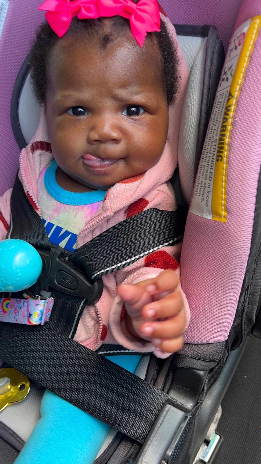 Jenesis joined the competition — help win amazing prizes! baby, child, car_seat, pink_bow, blue_clothing, seatbelt, toy, pacifier, infant, cute, tongue_out, playful, close_up, indoors, safety, person, smiling, jacket, hand, happy