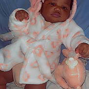 Jenesis is registered to the contest to win money with this photo: baby, infant, child, soft_toy, plush, robe, hood, ears, floral_pattern, white, peach, bed, pillow, blanket, socks, cute, chubby, smiling, lying_down, indoor