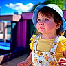 toddler, child, sunhat, blue_sky, outdoor, daylight, smiling, yellow_clothing, floral_pattern, playground, wooden_deck, happy, cute, portrait, summer, person, baby, curly_hair, sunlight, nature