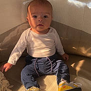Jonas participe au concours pour gagner de l'argent avec cette photo : baby, child, infant, couch, sitting, clothing, white_shirt, blue_pants, yellow_shoes, red_star, indoor, face, expression, person, furniture, sunlight, shadow, curious, wide_eyes, home