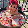 Audrey is registered to the contest to win money with this photo: baby, child, milk_bath, strawberries, red_bow, headband, wooden_tub, outdoor, sunlight, smiling, happy, foot, water, fruit, balcony, railing, concrete_floor, parked_cars, greenery, person