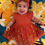 Audrey is registered to the contest to win money with this photo: baby, child, smiling, dress, headband, bow, orange, gold, polka_dots, blanket, floral, happy, cute, infant, portrait, lying_down, celebration, fabric, pattern, toddler