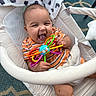 baby, infant, toy, colorful_toy, baby_rocker, striped_shirt, smile, happy, laughing, blanket, plush_toy, patterned_carpet, indoor, child, person, cushion, seat, hand, foot, head
