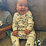 baby, child, smiling, onesie, whale_print, couch, indoor, happy, infant, cozy, sitting, clothing, person, furniture, blanket, cute, portrait, family, casual, home
