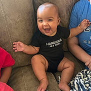 Cason is registered to the contest to win money with this photo: baby, child, couch, smiling, happy, black_onesie, clothing, person, family, indoor, furniture, arm, hand, foot, blanket, blue_shirt, skin, sitting, laughing, baby_face