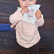 Lily-Rose a rejoint le concours — aidez-le/la à gagner de superbes lots ! toddler, child, indoor, headband, bow, smiling, holding, card, blue, pink_clothing, black_leggings, floor, couch, stone_wall, face, eyes, standing, barefoot, person, baby
