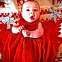 baby, infant, red_dress, blanket, reindeer_pattern, silver_bows, holiday, christmas, festive, cute, lying_down, expression, wide_eyes, small_hands, cozy, soft_texture, indoors, person, portrait, holiday_season