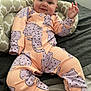baby, bed, child, cozy, cute, face, hand, happy, indoors, infant, onesie, patterned_clothing, peach, person, pillow, portrait, purple, resting, smile, soft_fabric