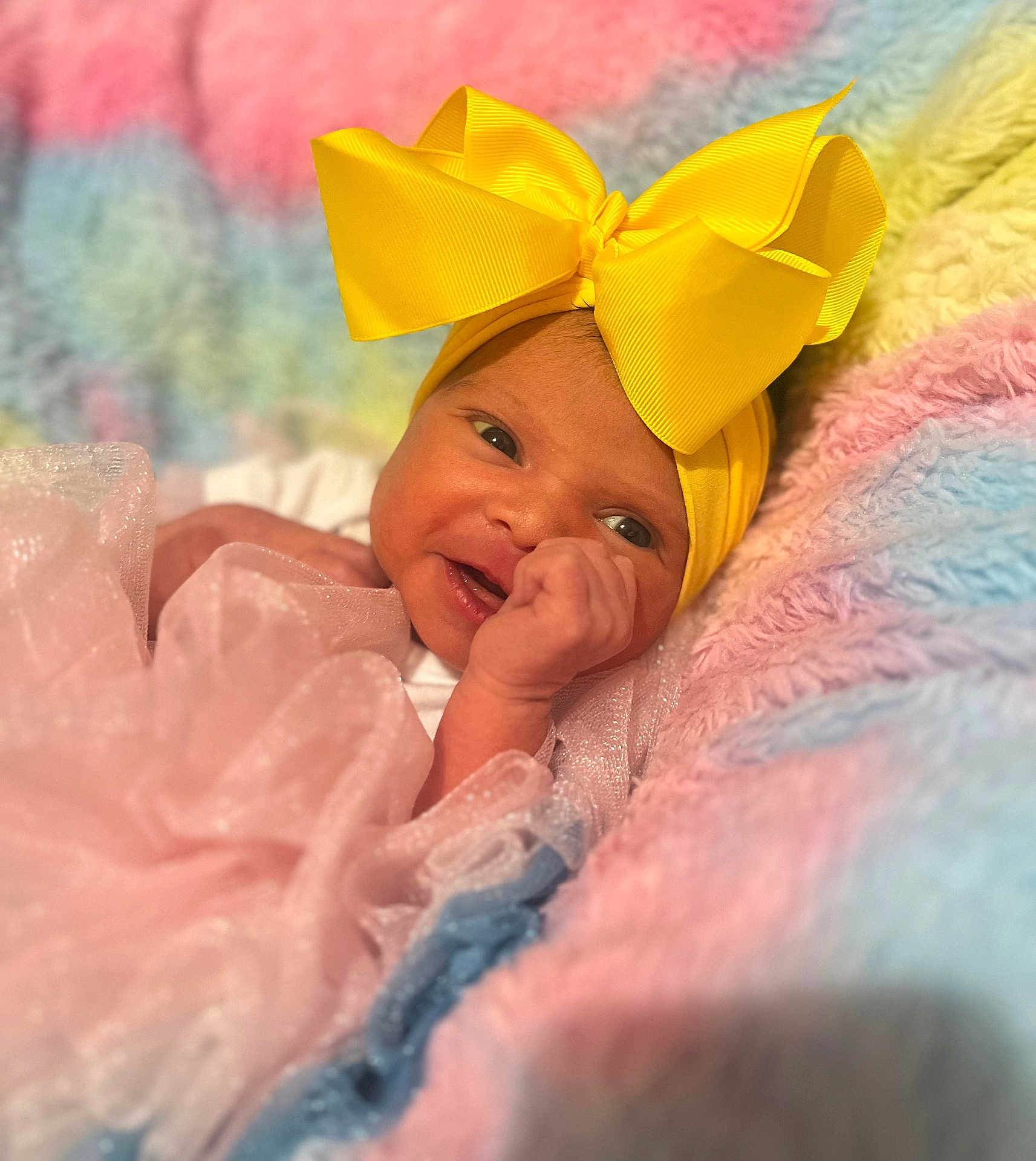 Julie is registered to the contest to win money with this photo: baby, infant, yellow_bow, headband, pink_dress, blanket, pastel_colors, soft_texture, smile, face, cute, newborn, child, portrait, closeup, happy, lying_down, cozy, fabric, toddler