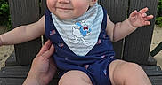 Walter is registered to the contest to win money with this photo: baby, child, smiling, blue_outfit, bib, donald_duck, bench, wooden_bench, hand, outdoor, grass, cute, happy, person, infant, sitting, skin, foot, arm, face