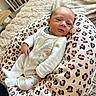 baby, newborn, infant, onesie, leopard_print, baby_pillow, giraffe_print, blanket, indoor, soft_texture, shelf, books, cozy, cute, child, person, portrait, relaxing, home, comfort