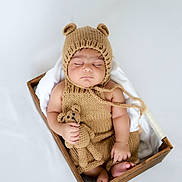 Divansh Prasad is registered to the contest to win money with this photo: baby, sleeping, knitted_clothing, bear_hat, wooden_box, blanket, soft_toy, teddy_bear, infant, cute, peaceful, portrait, newborn, hand, foot, indoors, cozy, child, hat, knitwear
