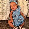 baby, child, smiling, blue_dress, headband, floral_pattern, couch, indoor, happy, footwear, sandals, infant, cute, portrait, sitting, skin, hand, face, person, cozy