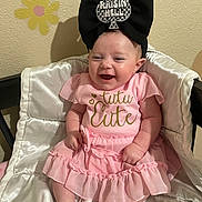Khloe-Jo joined the competition — help win amazing prizes! baby, infant, pink_dress, headband, black_bow, smile, sitting, cushion, satin, wall, flower_decals, cute, happy, indoors, child, clothing, person, headwear, joyful, portrait