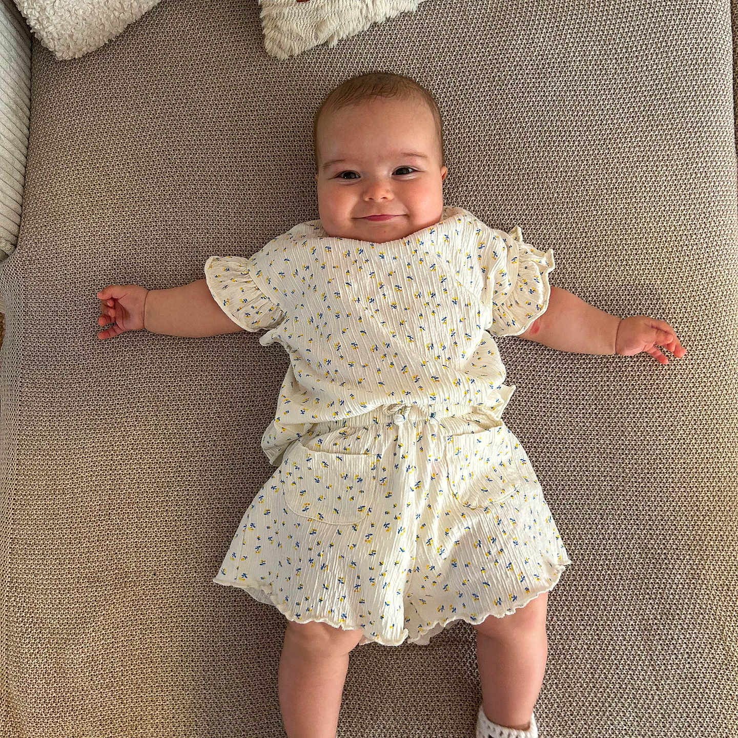 Romy a rejoint le concours — aidez-le/la à gagner de superbes lots ! baby, blanket, child, comfort, couch, cute, fabric, floral_outfit, happy, indoor, infant, knitted_shoes, lying_down, person, pillow, relaxing, smiling, soft, texture, young