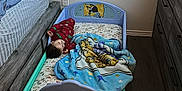 Noah is registered to the contest to win money with this photo: toddler, bed, blanket, pajamas, floor, dresser, curtain, wall, room, sleeping, child, furniture, indoors, cozy, blue, red, wooden_floor, pillow, toy, blanket_pattern