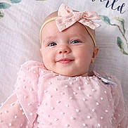 Ellie is registered to the contest to win money with this photo: baby, infant, child, headband, bow, pink_dress, textured_fabric, smile, face, eyes, lying_down, blanket, bedding, portrait, soft_texture, cute, close_up, skin, happy, decorative_text