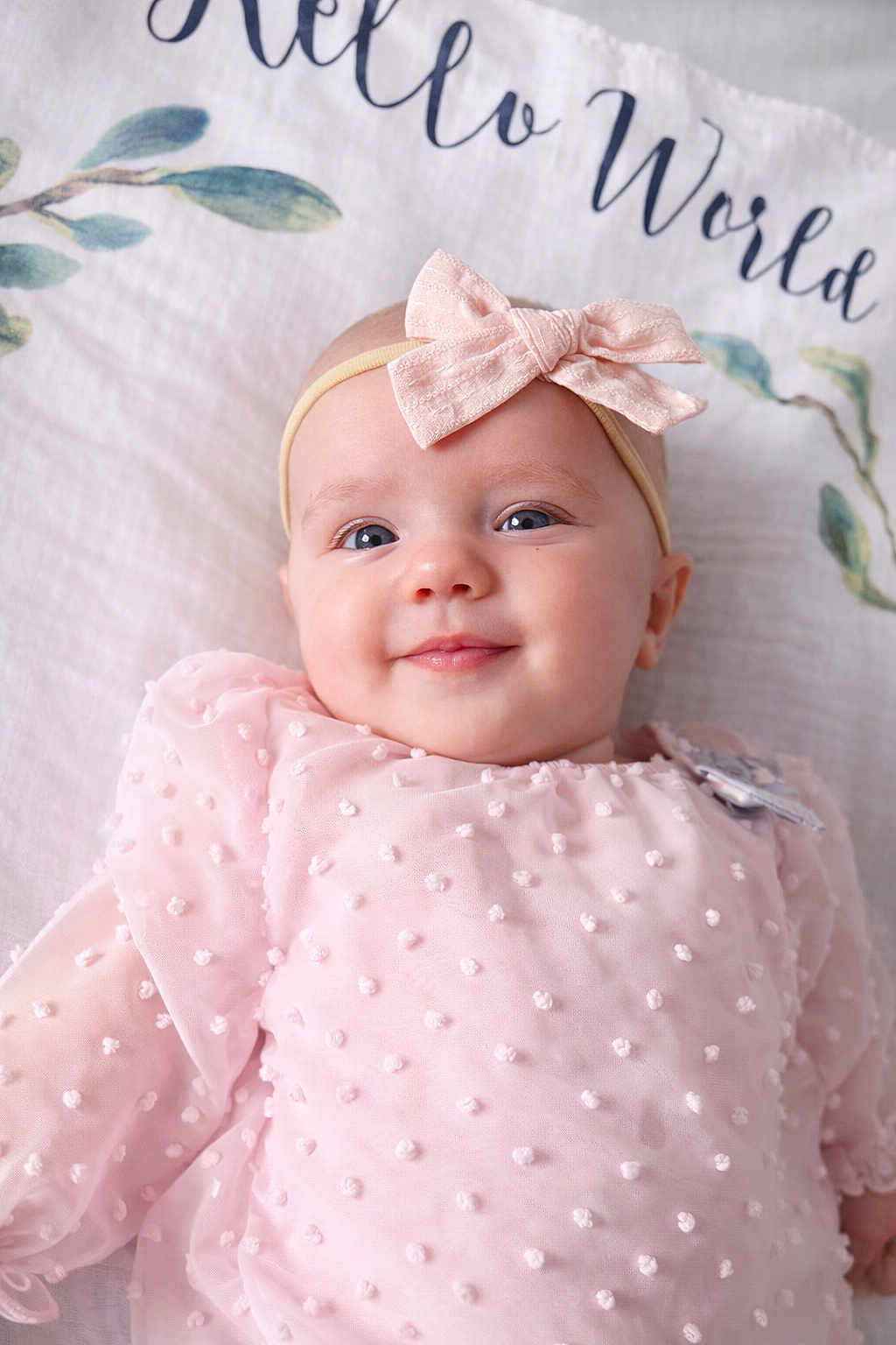 Ellie is registered to the contest to win money with this photo: baby, infant, child, headband, bow, pink_dress, textured_fabric, smile, face, eyes, lying_down, blanket, bedding, portrait, soft_texture, cute, close_up, skin, happy, decorative_text