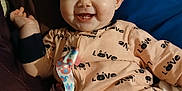 Hope is registered to the contest to win money with this photo: baby, smiling, onesie, love_print, pacifier_clip, toy, bed, pillow, indoor, child, happy, cute, infant, clothing, person, face, relaxing, cheerful, comfort, playful