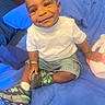 toddler, child, smile, indoor, bed, blue_bedspread, white_tshirt, denim_shorts, sneakers, happy, cute, person, young_child, casual_clothing, seated, bracelet, toy, comfort, portrait, candid