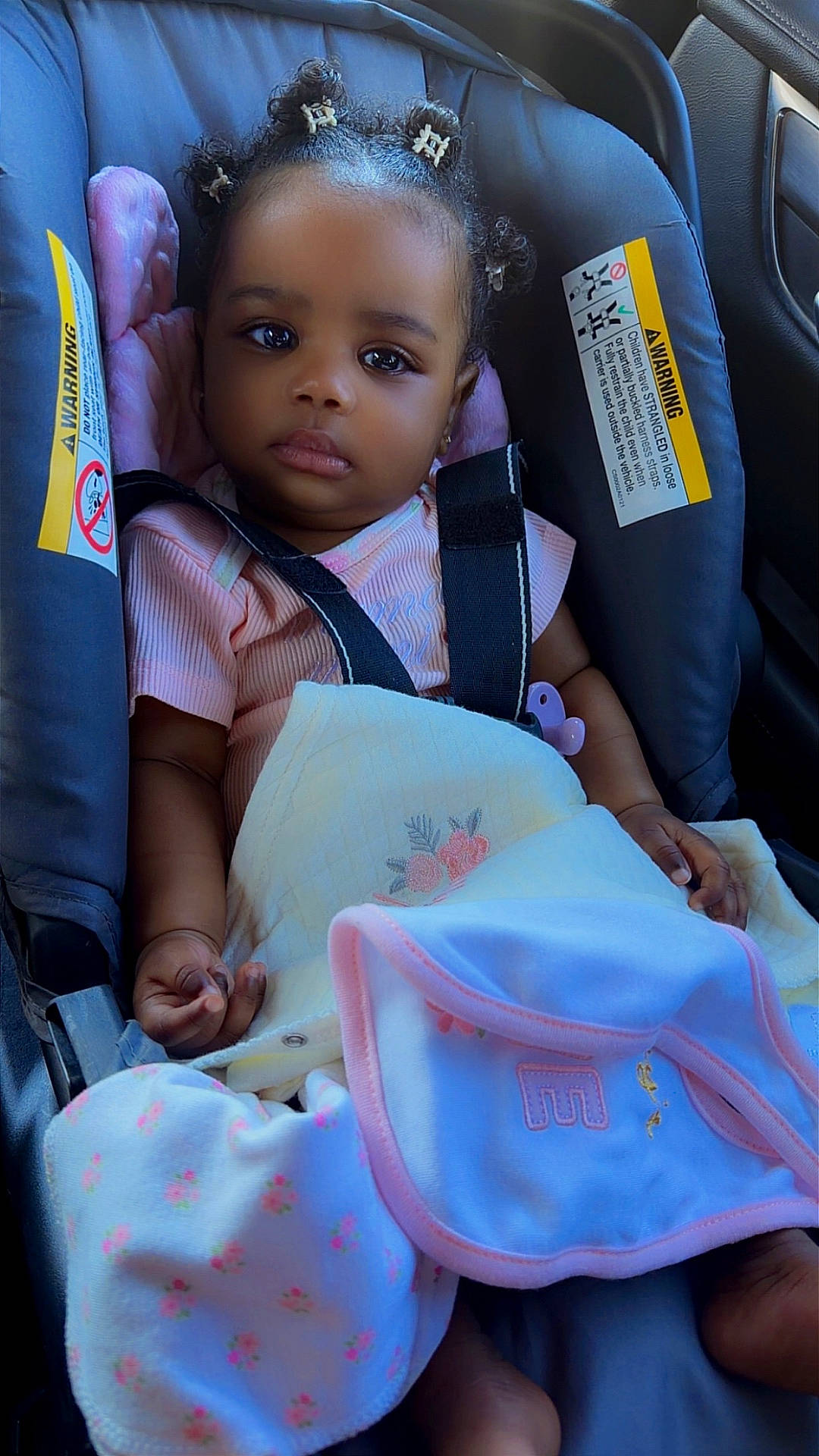 Zaira Kerène Victor is registered to the contest to win money with this photo: baby, blanket, buckled, car, car_seat, child, dark_skin, hair_buns, harness, indoors, infant, looking_at_camera, passenger, pink_clothing, portrait, safety_warning, sitting, soft_blanket, travel, vehicle