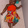 baby, child, infant, crib, nursery, portrait, lying_down, orange_outfit, colorful_dress, floral_pattern, sandals, plush_toys, stuffed_animal, pink_blanket, mattress, baby_care, overhead_view, indoors, smiling, fashionable
