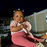Zaira Kerène Victor is registered to the contest to win money with this photo: baby, child, infant, portrait, sitting, outdoor, night, backyard, playground, pink_clothing, leggings, shoes, hair_clips, flower_accessories, serious_expression, flash_photography, fence, party, play_equipment, family_photo