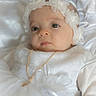 baby, infant, white_dress, flower_headband, gold_necklace, portrait, soft_lighting, close_up, cute, child, newborn, satin_background, decorative_clothing, peaceful, young_child, face, headwear, indoors, small_person, baby_girl