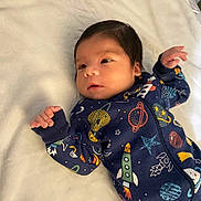 Josiah is registered to the contest to win money with this photo: baby, infant, onesie, space_theme, rocket, planet, stars, blanket, lying_down, cute, child, sleepwear, young, portrait, indoor, soft_texture, hand, face, expression, cozy