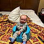 baby, child, smiling, blue_baby_seat, bed, blanket, pillow, gray_outfit, purple_socks, wooden_headboard, indoor, remote_control, bedroom, furniture, person, home, happy, sitting, young_child, portrait