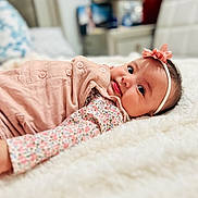 Eliana is registered to the contest to win money with this photo: baby, infant, girl, lying_down, blanket, headband, flower, pink_clothing, floral_pattern, bedroom, soft_texture, cute, portrait, face, child, indoors, cozy, smile, closeup, comfortable