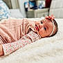 baby, infant, girl, lying_down, blanket, headband, flower, pink_clothing, floral_pattern, bedroom, soft_texture, cute, portrait, face, child, indoors, cozy, smile, closeup, comfortable