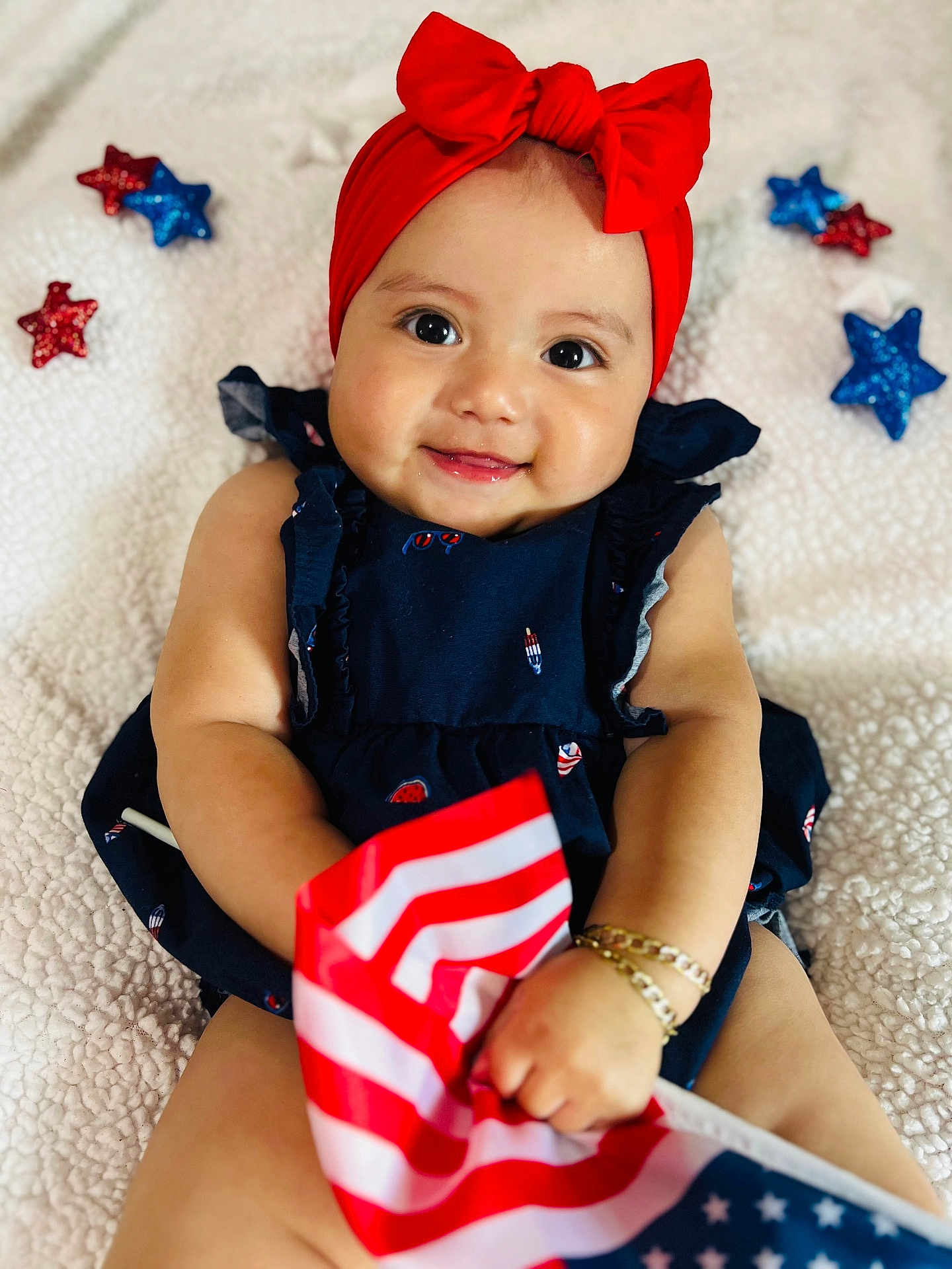 Eliana joined the competition — help win amazing prizes! baby, smiling, red_headband, bow, navy_blue_dress, american_flag, bracelets, sitting, white_blanket, stars, glitter, cute, portrait, infant, happy, celebration, holiday, indoors, closeup, child