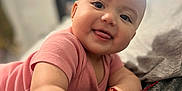 Eliana joined the competition — help win amazing prizes! baby, smiling, tongue_out, pink_shirt, arm, hand, blanket, indoor, face, person, child, cute, lying_down, happy, young_child, bedroom, soft_lighting, cozy, infant, portrait