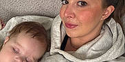 Lottie is registered to the contest to win money with this photo: woman, baby, sleeping, couch, hoodie, face, person, relaxing, indoor, closeup, casual_clothing, comfort, resting, portrait, head, brown_hair, skin, expression, young_child, family