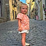 toddler, child, street, cobblestone, shoes, shorts, shirt, pony_tail, outdoor, daylight, building, sidewalk, curious, person, walking, summer, urban, fashion, young_child, casual