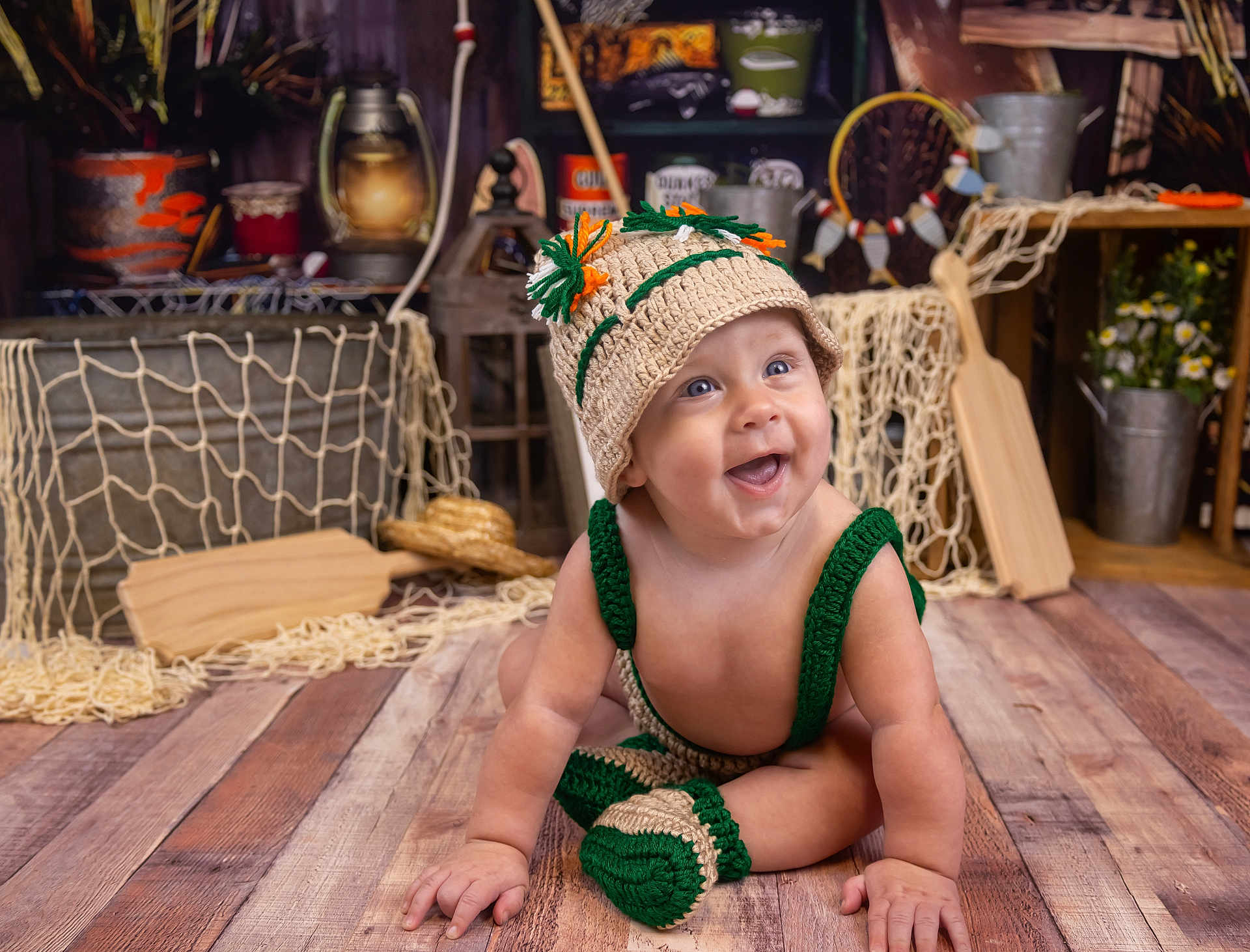 Weston joined the competition — help win amazing prizes! baby, child, smiling, knitted_hat, knitted_clothing, wooden_floor, rustic_decor, fishing_net, wooden_paddle, metal_bucket, flowers, indoor, cute, happy, sitting, portrait, floor, decor, hat, playful