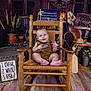baby, child, rocking_chair, wooden_chair, brown_outfit, fish_patch, smiling, indoor, rustic, fishing_theme, fishing_net, lantern, wooden_floor, sign, plants, hat, bucket, happy, portrait, crawling_steps