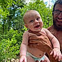 Weston is registered to the contest to win money with this photo: baby, infant, man, adult, glasses, beard, diaper, smile, happy, outdoor, nature, trees, greenery, rocks, creek, hand, person, holding, portrait, summer