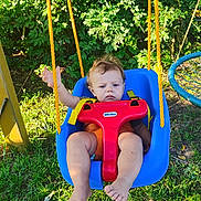Charles is registered to the contest to win money with this photo: toddler, baby, swing, outdoor, grass, greenery, playground, child, seat, yellow_straps, red_plastic, blue_swing, barefoot, sunlight, nature, play, young_child, expression, summer, park