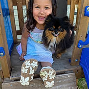 Kelanah is registered to the contest to win money with this photo: child, girl, dog, pet, playground, wooden_structure, sandals, braided_hair, smiling, happy, outdoor, grass, sunlight, playtime, cute, animal, friendship, portrait, young, fun