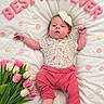 baby, baby_clothing, best_mom_ever, celebration, cute, decor, flower_bouquet, happy, headband, indoor, infant, lying_down, newborn, pink_pants, polka_dots, portrait, quilt, soft_lighting, text_overlay, tulips