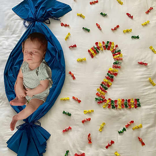 Phoenix is registered to the contest to win money with this photo: baby, sleeping, blue_fabric, candy_wrapper, number_two, colorful_candy, white_sheet, milestone, celebration, infant, cute, resting, wrapped, small_child, soft_lighting, indoors, decorative, creative, peaceful, portrait