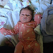 Phoenix is registered to the contest to win money with this photo: baby, newborn, infant, pink_onesie, floral_pattern, blanket, mattress, bed, soft_fabric, lying_down, cute, face, hair, indoors, child, person, sleepwear, cozy, resting, portrait