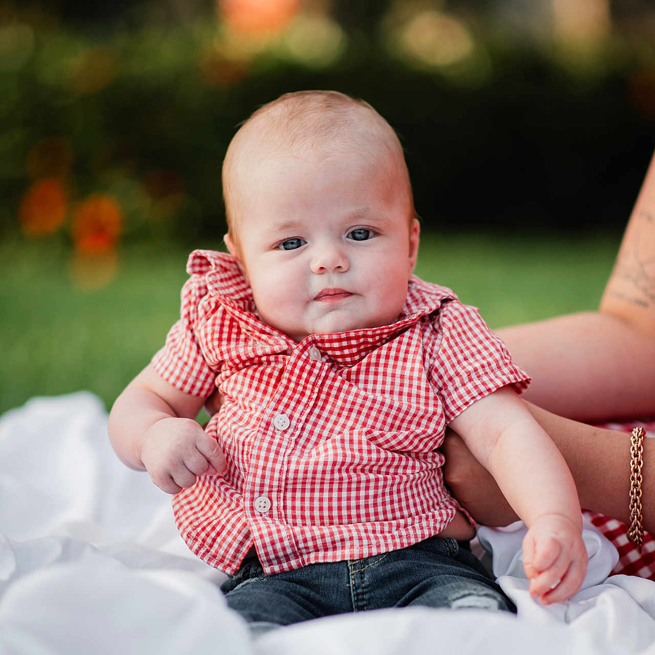 Jensen Cole is registered to the contest to win money with this photo: baby, child, infant, red_checkered_shirt, jeans, white_blanket, outdoor, grass, bokeh, tattoo, bracelet, arm, person, portrait, cute, smiling, sitting, nature, sunlight, support