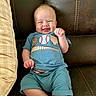 baby, smiling, blue_clothing, baseball_theme, couch, leather, pillow, happy, sitting, infant, cute, child, indoors, portrait, young, person, casual, relaxed, funny_face, expression