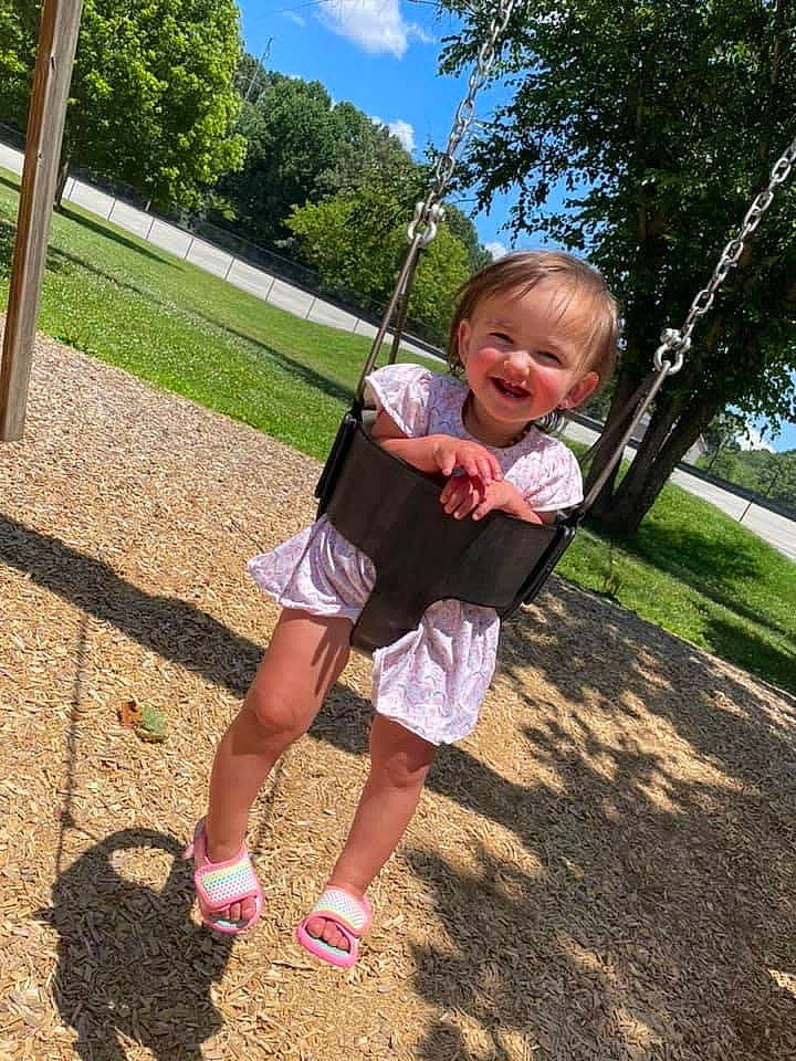Madalynn is registered to the contest to win money with this photo: baby, child, city, cloud, fun, grass, happy, human_settlement, joy, lawn, leisure, outdoor_play_equipment, people_in_nature, person, plant, playground, recreation, sky, smile, swing