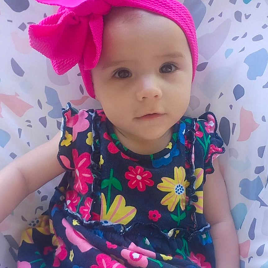 Dahlia joined the competition — help win amazing prizes! baby, child, girl, headband, pink_bow, dress, floral_pattern, seat, cushion, outdoor, grass, portrait, cute, infant, sitting, colorful, person, face, young_child, headwear