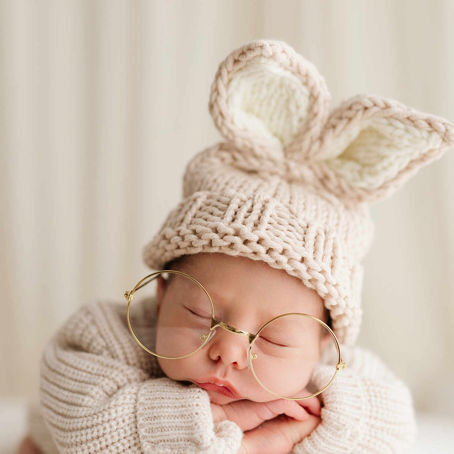 Aiden joined the competition — help win amazing prizes! baby, sleeping, glasses, knitted_hat, bunny_ears, cute, soft_lighting, neutral_background, cozy, portrait, infant, resting, closeup, warm_colors, child, adorable, knitwear, peaceful, hands, face